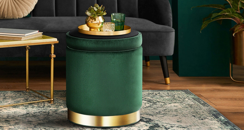 An Artiss green velvet ottoman with gold plating, holding a gold trinket tray with matching glasses and a pot plat in a gold vase.