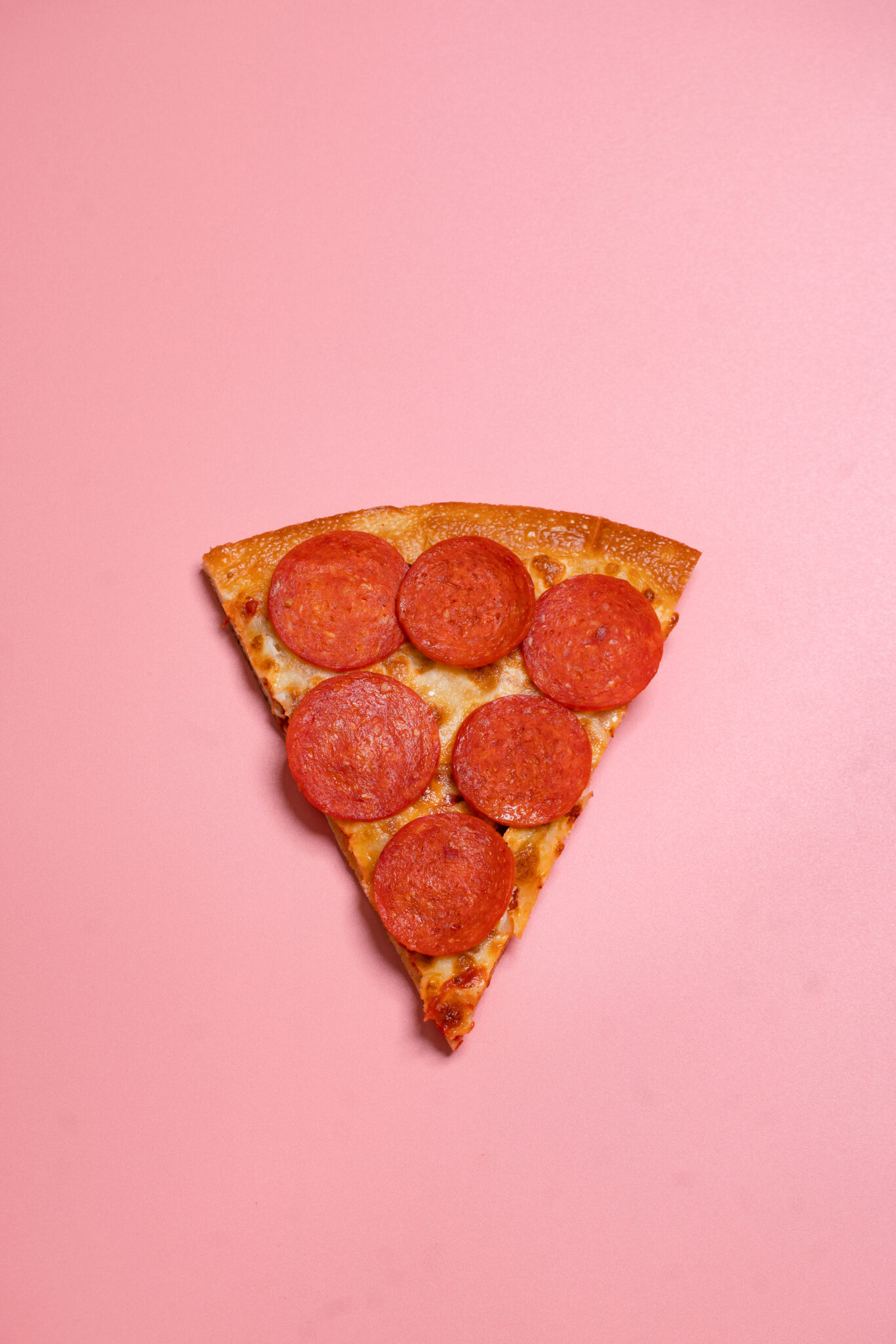 Commercial photo of slice of pizza against a pink background