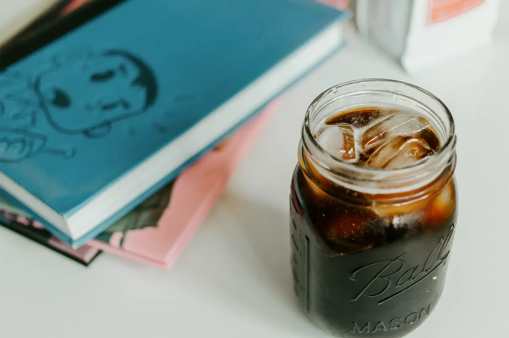 Cold brew coffee in a glass jar on a white table with notebooks stacked on one another at the side.