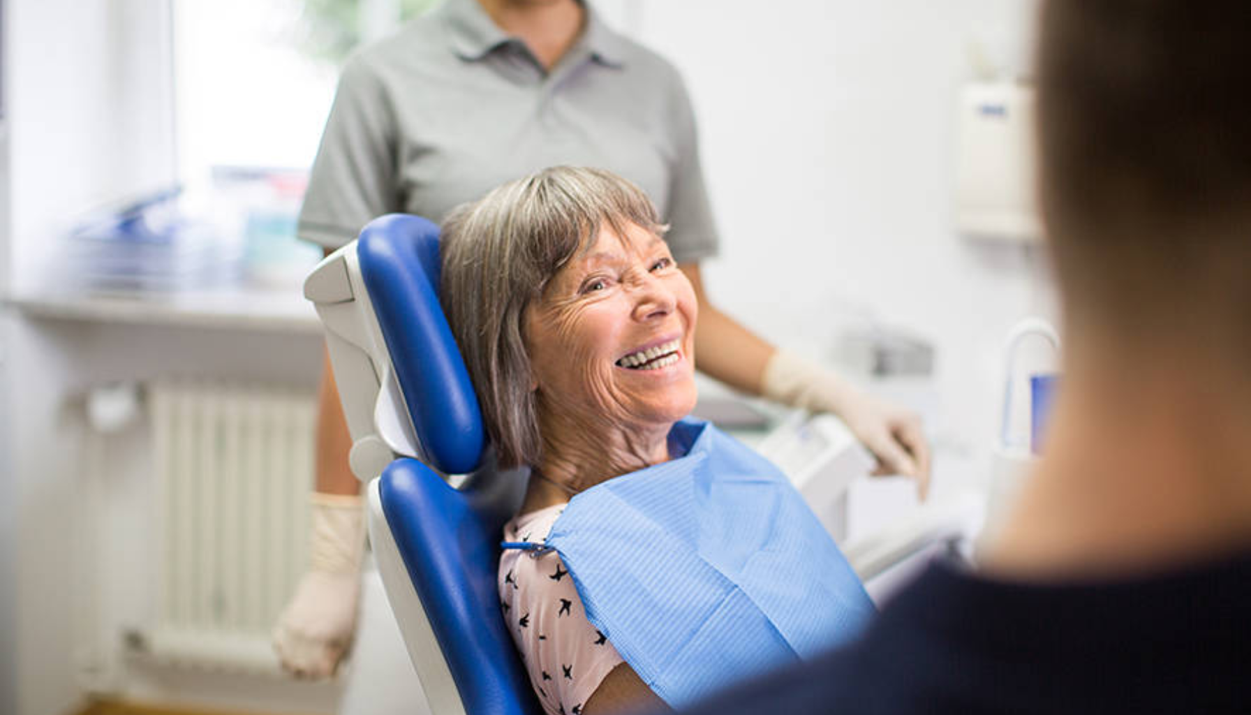 Smilende pasient i tannlegestol omgitt av tannhelsepersonell.