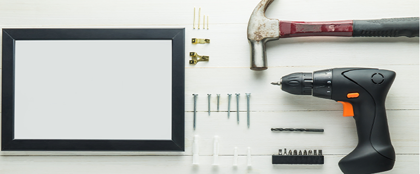 A picture frame and hanging tools, including a hammer, drill, drill bits, plastic anchors, screws, hooks and nails.