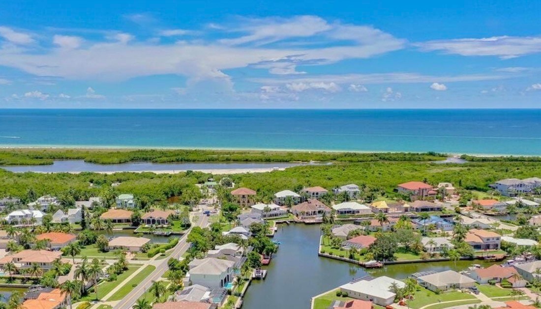 This image depicts a luxury waterfront home in the prestigious Tigertail neighborhood of Marco Island, featuring a private dock with boats moored nearby and serene canal waters. The contemporary masterpiece offers breathtaking views, embodying the ultimate island lifestyle with quick access to the open Gulf waters and pristine beaches.