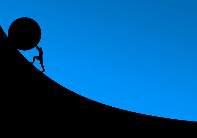 Silhouette of a person pushing a large boulder uphill against a bright blue background.