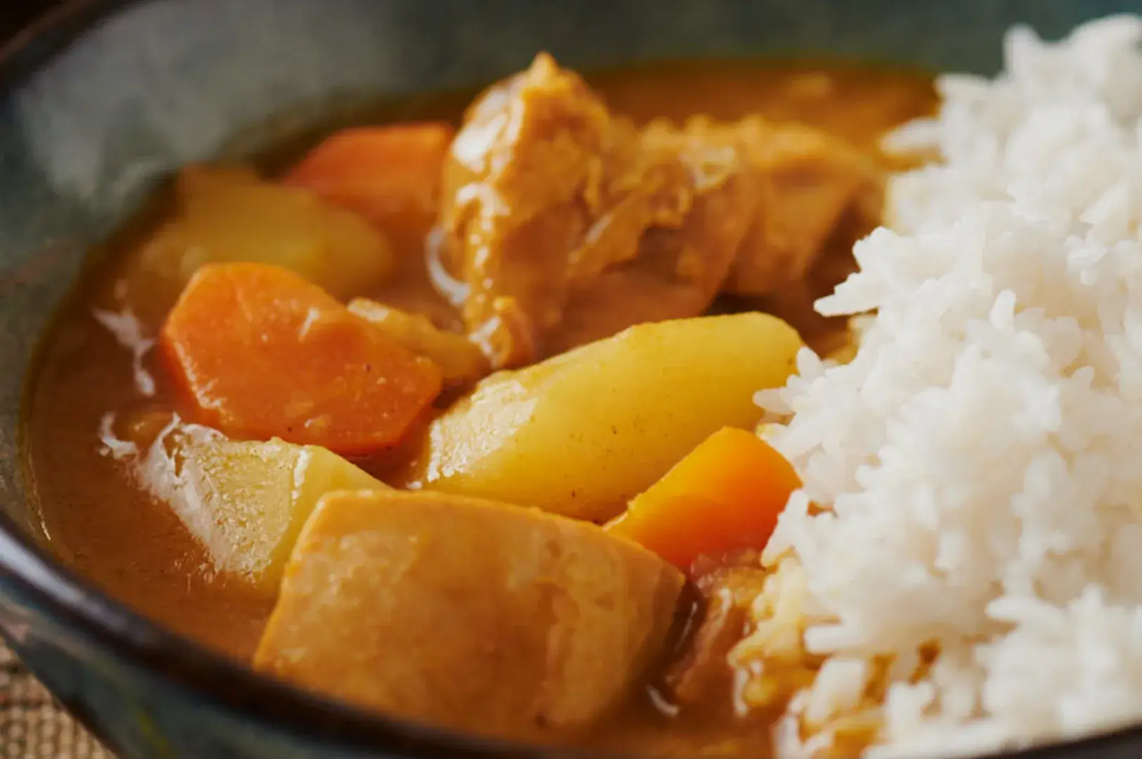 A bowl of curry with vegetables and pieces of meat, served alongside a portion of white rice.