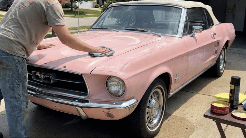 A man is waxing the pink car.