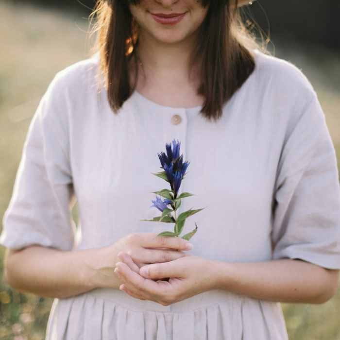 Woman holding a blue gentian flower, symbolising calm and healing, self-esteem.