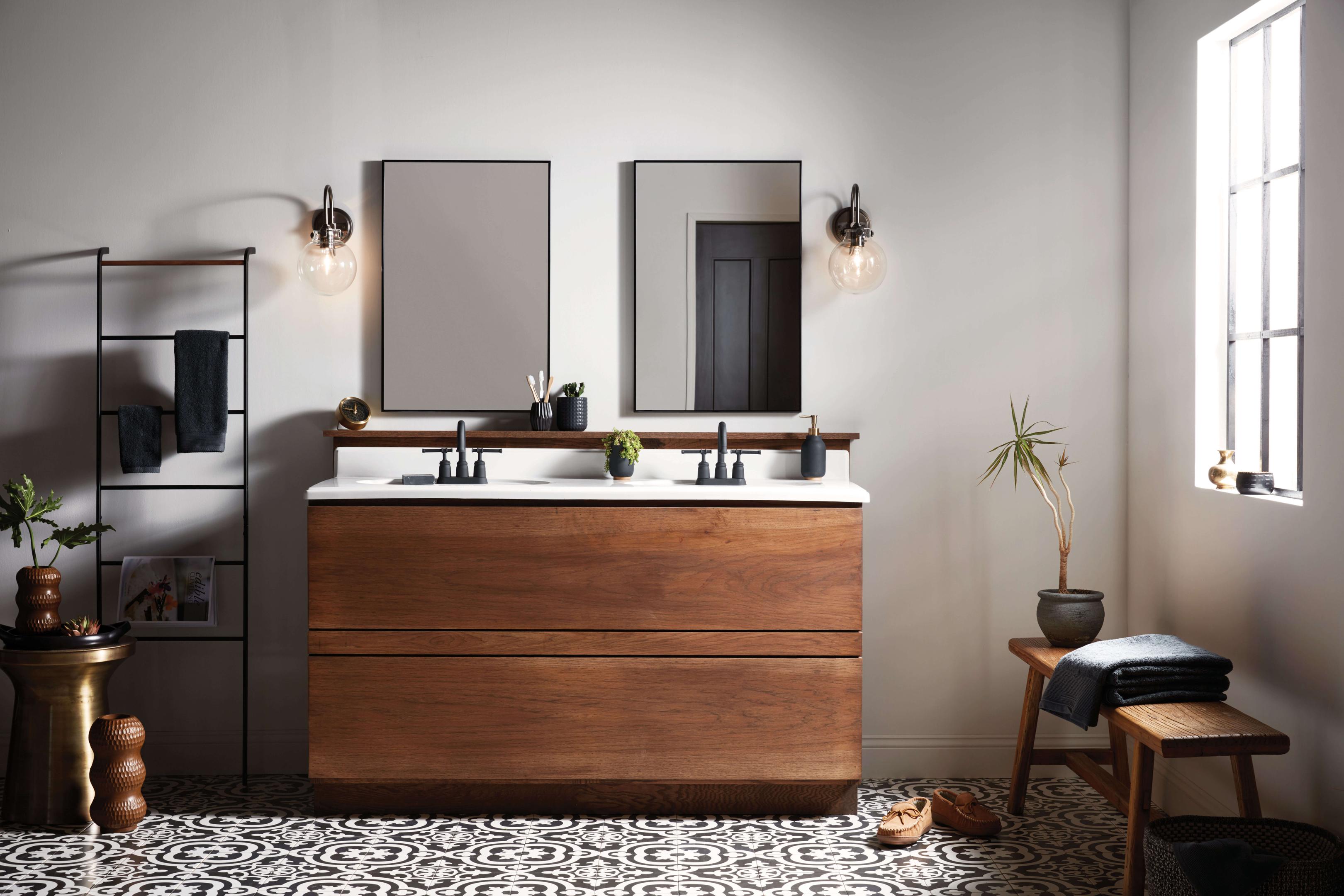 Matte black wall sconces beside the mirror with warm white energy efficient bulbs in a mid century modern bathroom with a wood cabinet vanity