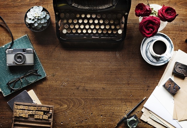 A writer's desk containing objects such as a typewriter, camera, and glasses.
