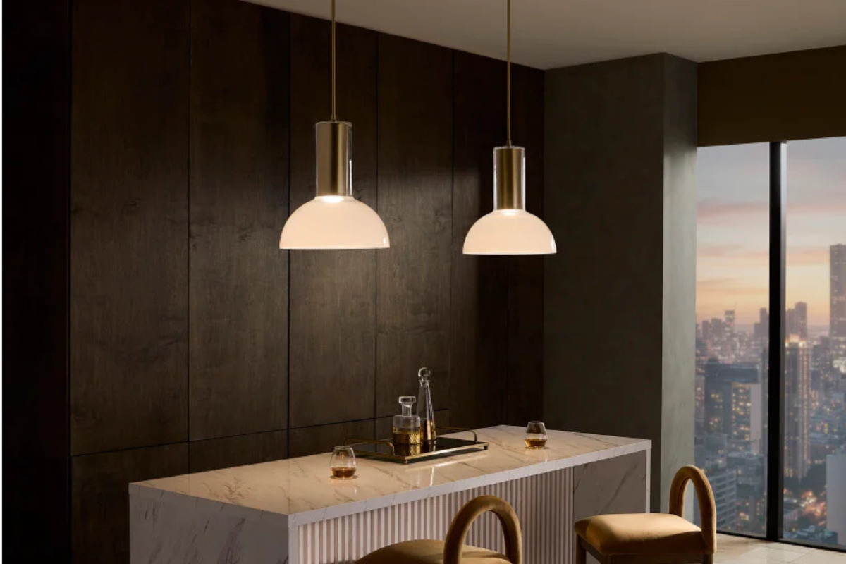 Brass pendant light fixtures over a white bar table, creating warm illumination and modern style with city views in the background.