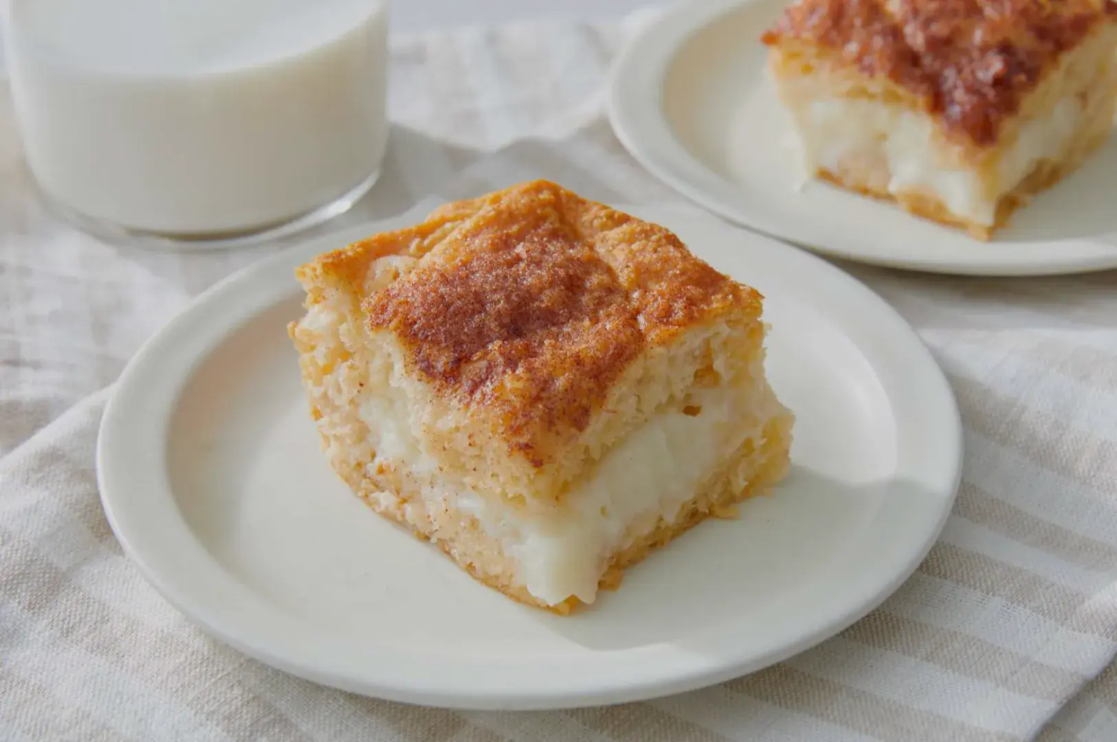 A slice of dessert on a plate, with a creamy filling and a golden-brown top, beside a glass of milk.