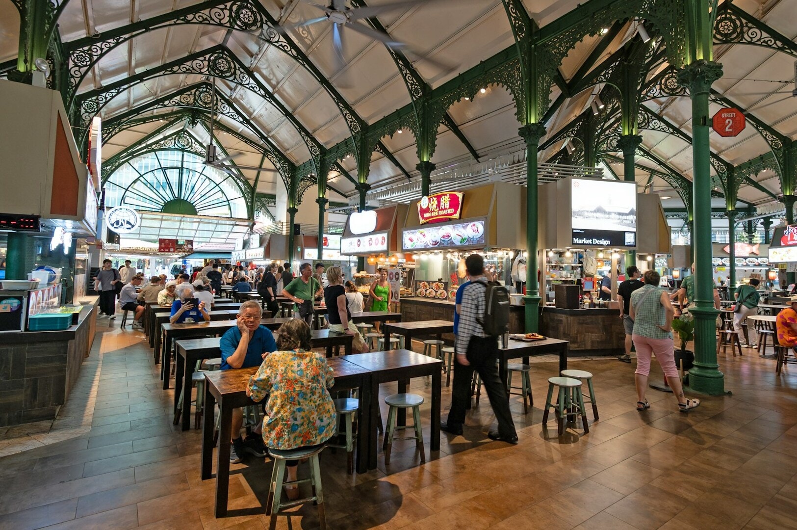 A vibrant indoor market scene with people dining and socializing in a busy hawker center atmosphere.