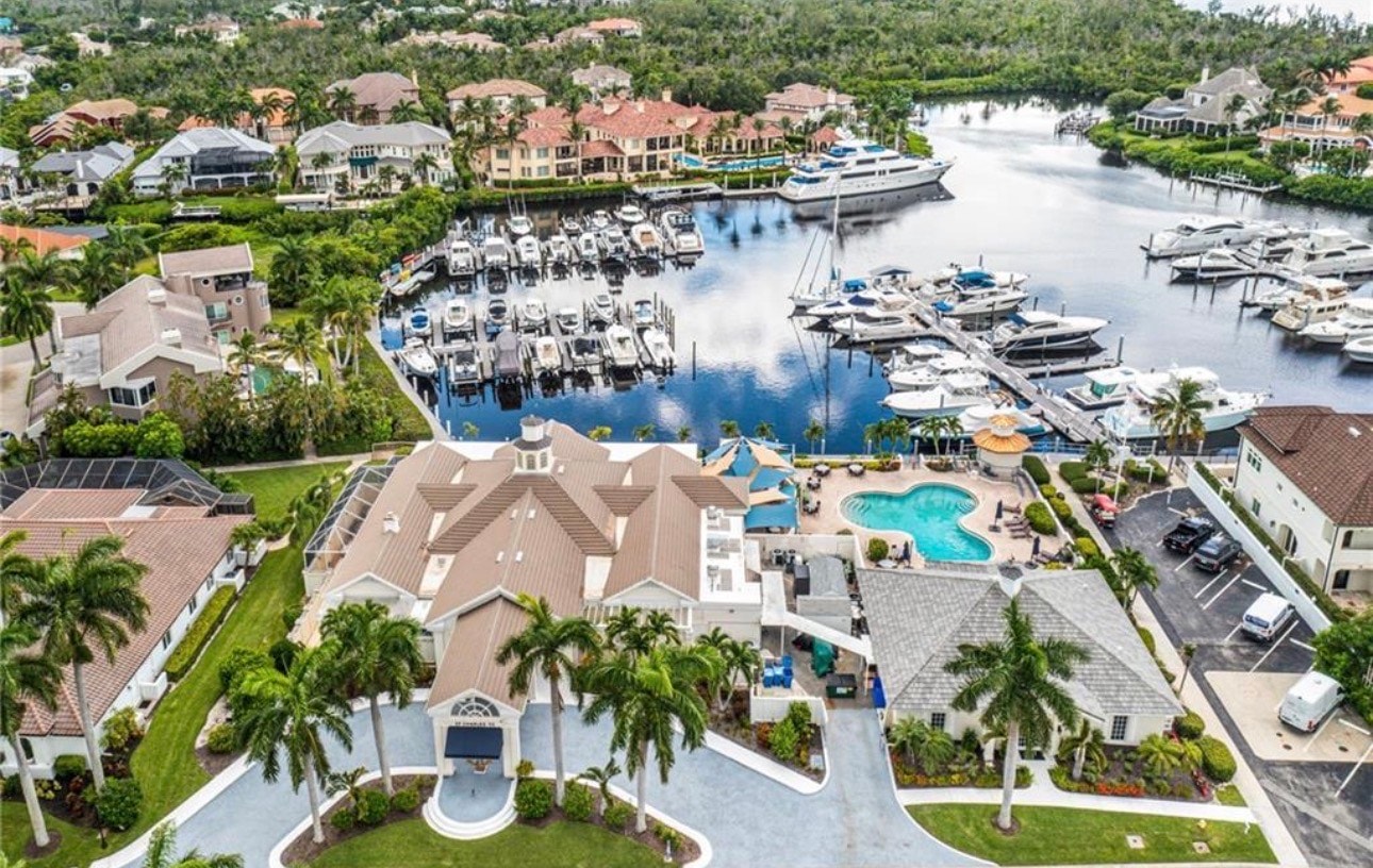 The image depicts a modern marina at St Charles Harbour in Fort Myers, featuring luxury yachts docked along the beautifully secluded natural harbor, which offers deep water access for boating enthusiasts. The scene captures the vibrant community atmosphere, with nearby dining options and social events at the Charles Yacht Club.