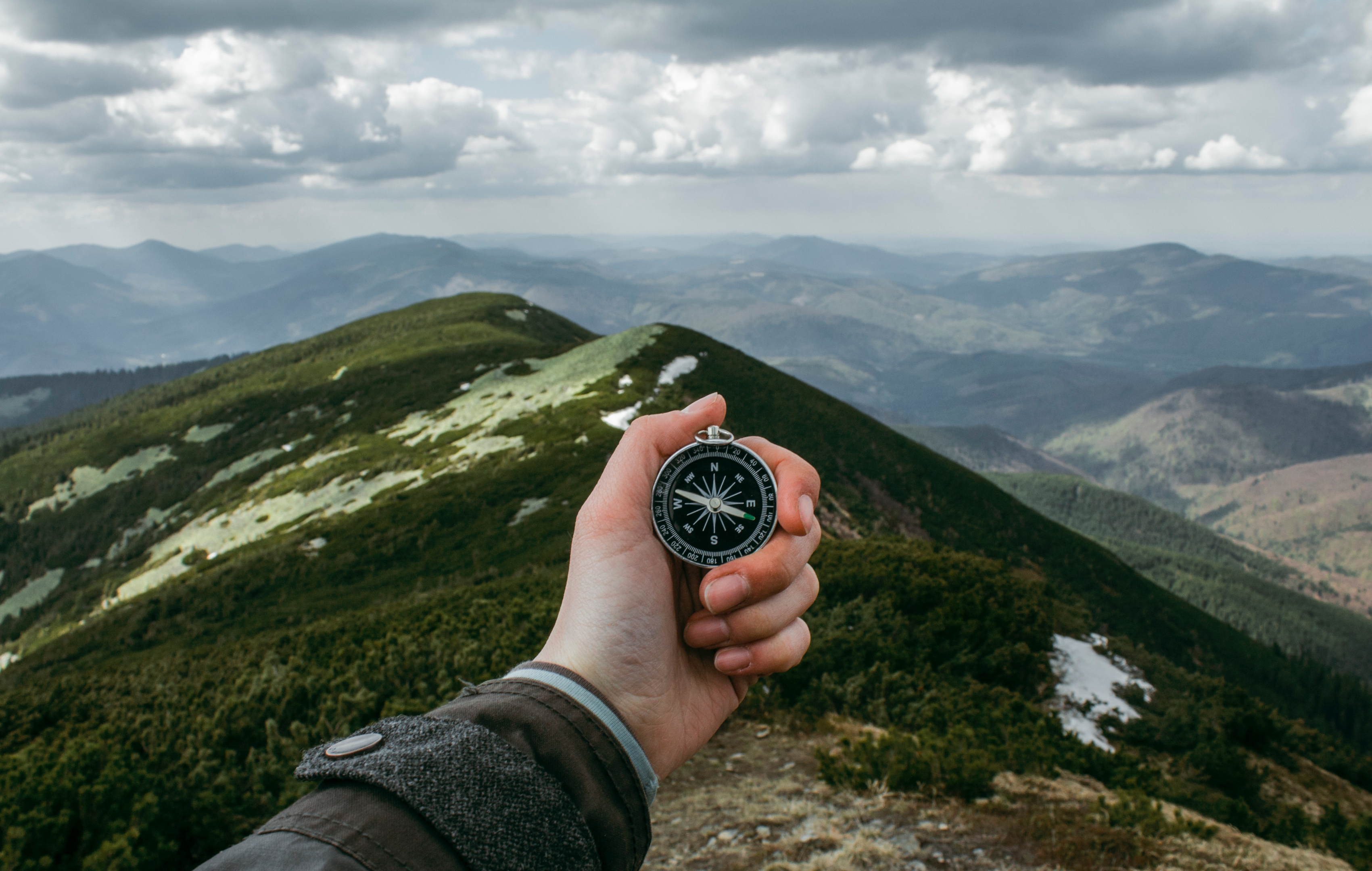 A hand holding up a compass over mountains