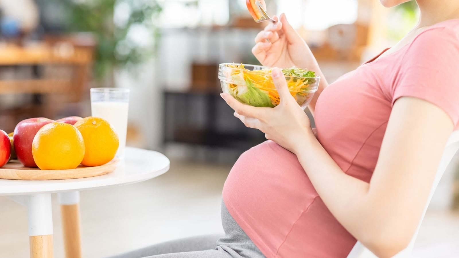 Pregnant woman in pink shirt eating fresh vegetable salad at home