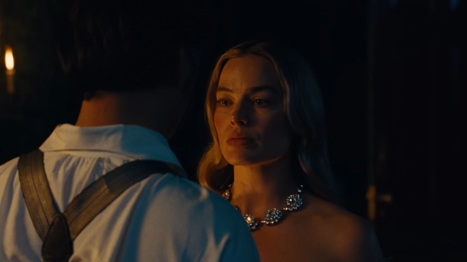 Margot Robbie as Catherine Earnshaw confronts mysterious man, necklace sparkling in warm candlelight in Wuthering Heights