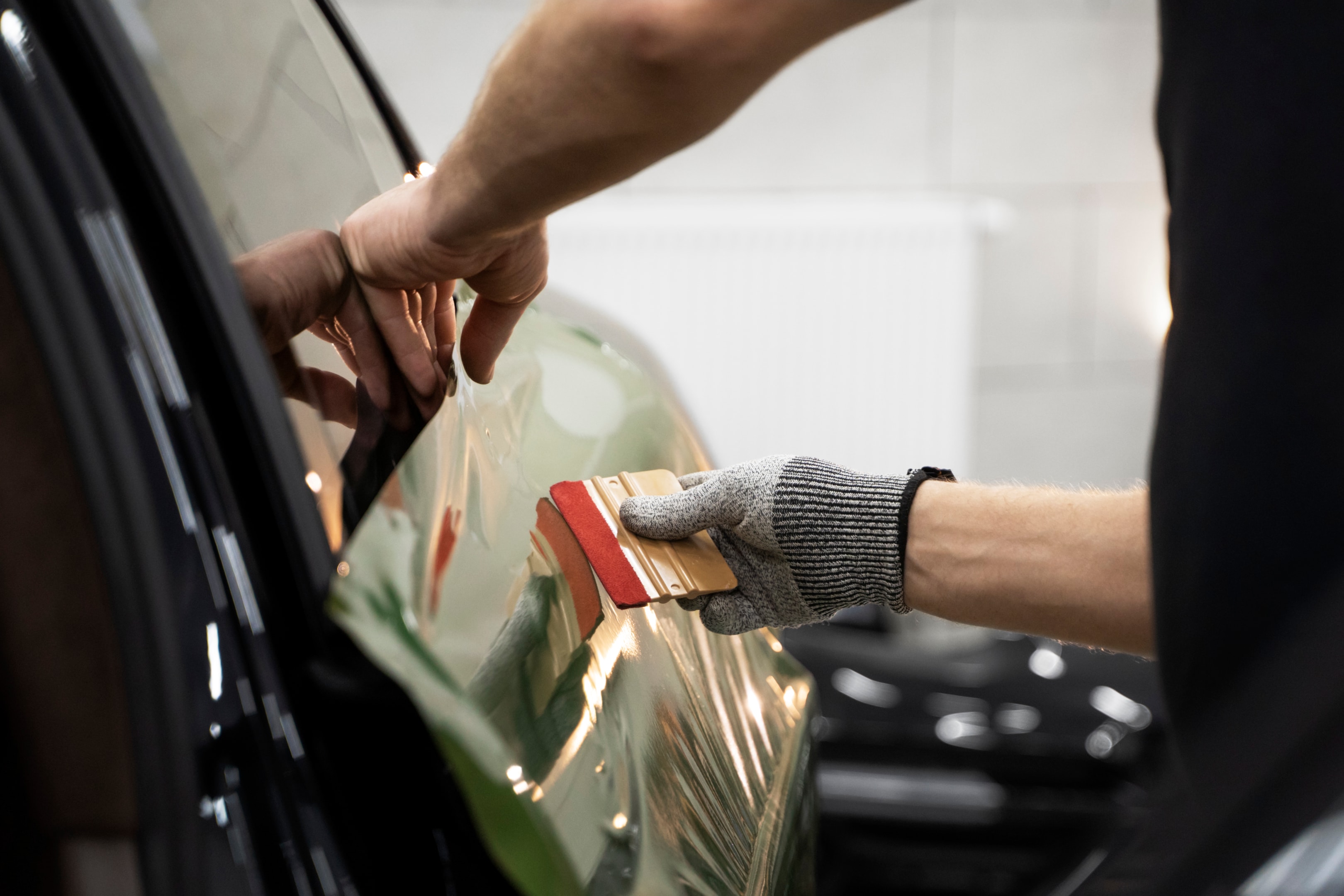 Close-up of a person wearing gloves installing a green vinyl wrap on a vehicle using a squeegee tool, highlighting the car wrapping process.