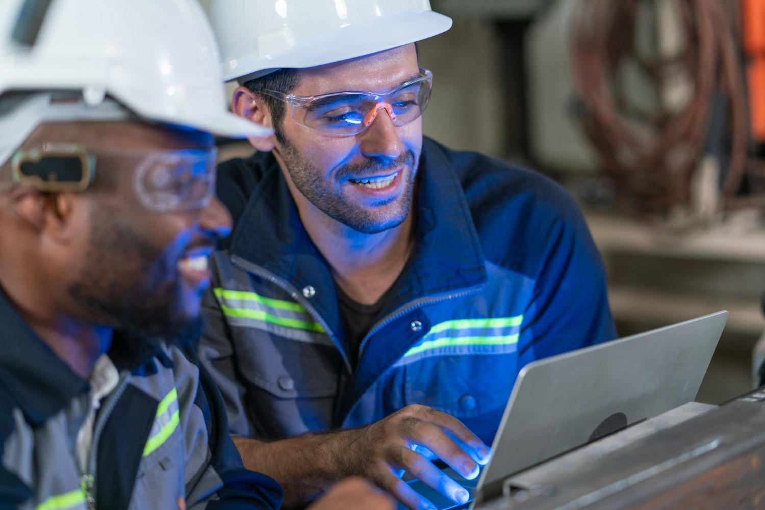 Two industrial workers in safety gear collaborate using a laptop, symbolizing the need for reliable phone systems in various industries. Their teamwork demonstrates the role of Tampa telecom solutions in facilitating telecom system upgrades for efficient operations.
