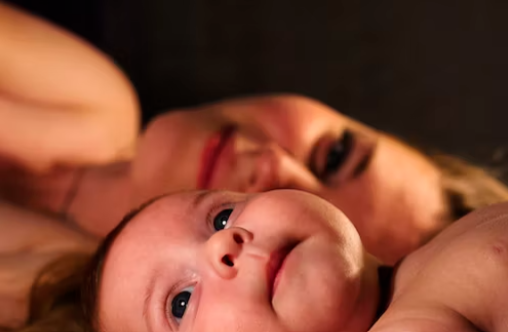 Baby lying on their back with Mum in background smiling