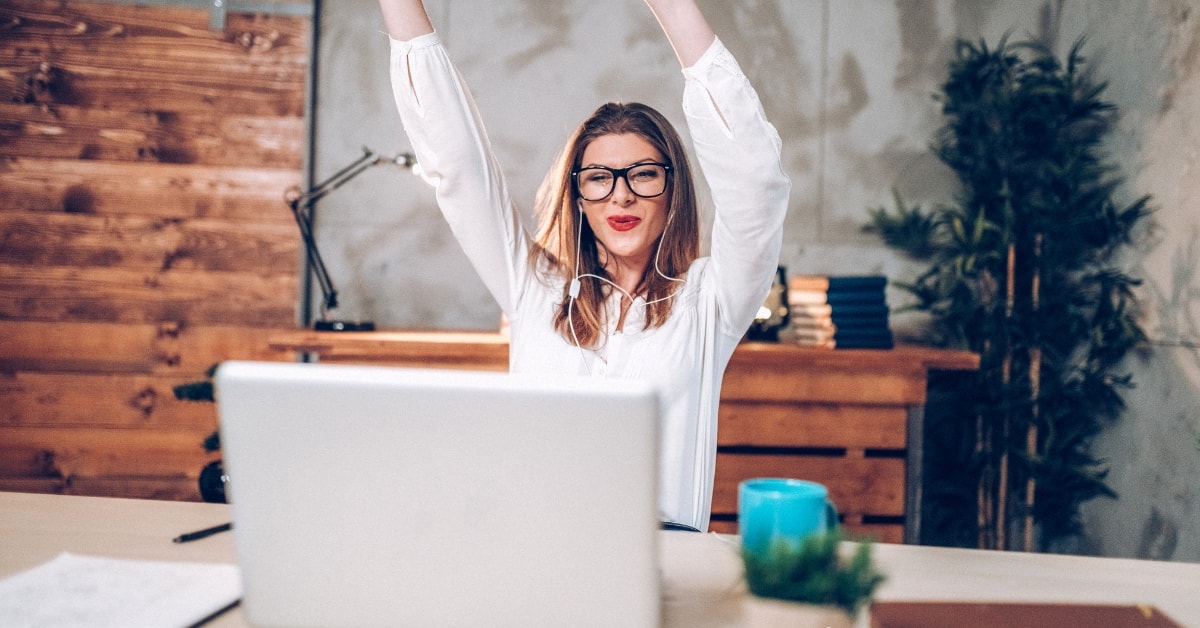 Smiling woman celebrating tax compliance success at her desk with a raised arm and laptop.