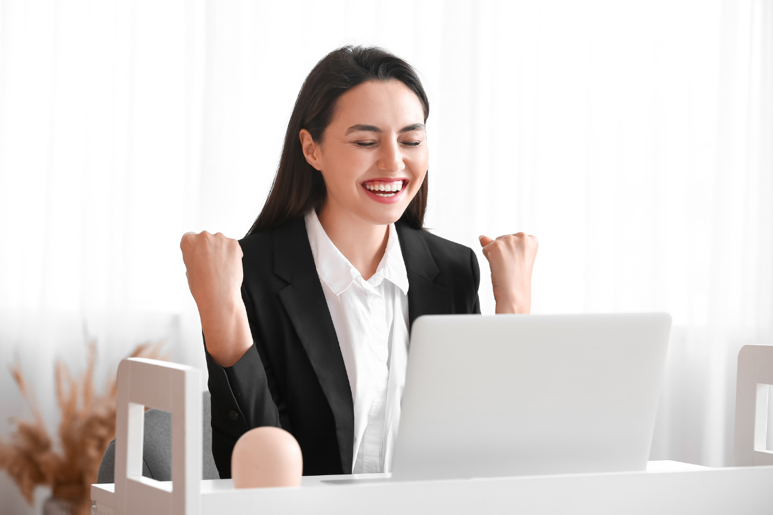 Smiling woman in business attire celebrating success in front of laptop during a virtual interview