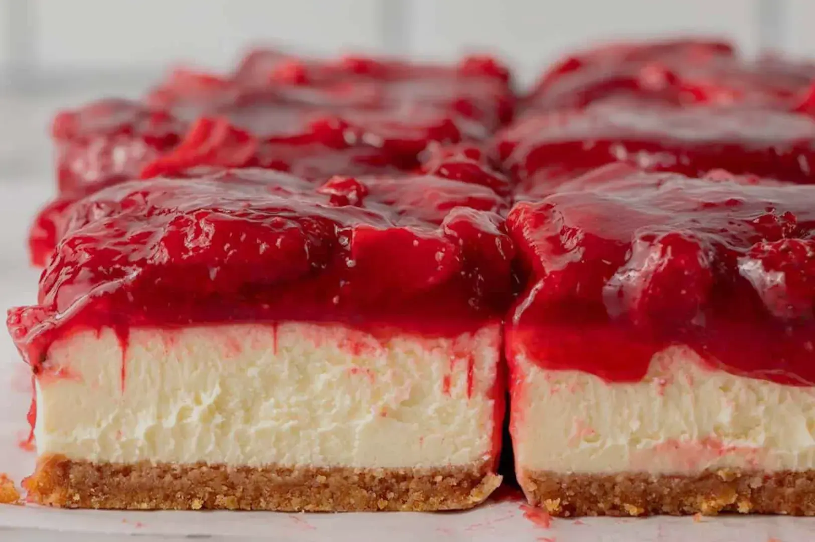 A close-up view of a dessert with a creamy white layer on a graham cracker crust, topped with a glossy red fruit filling.