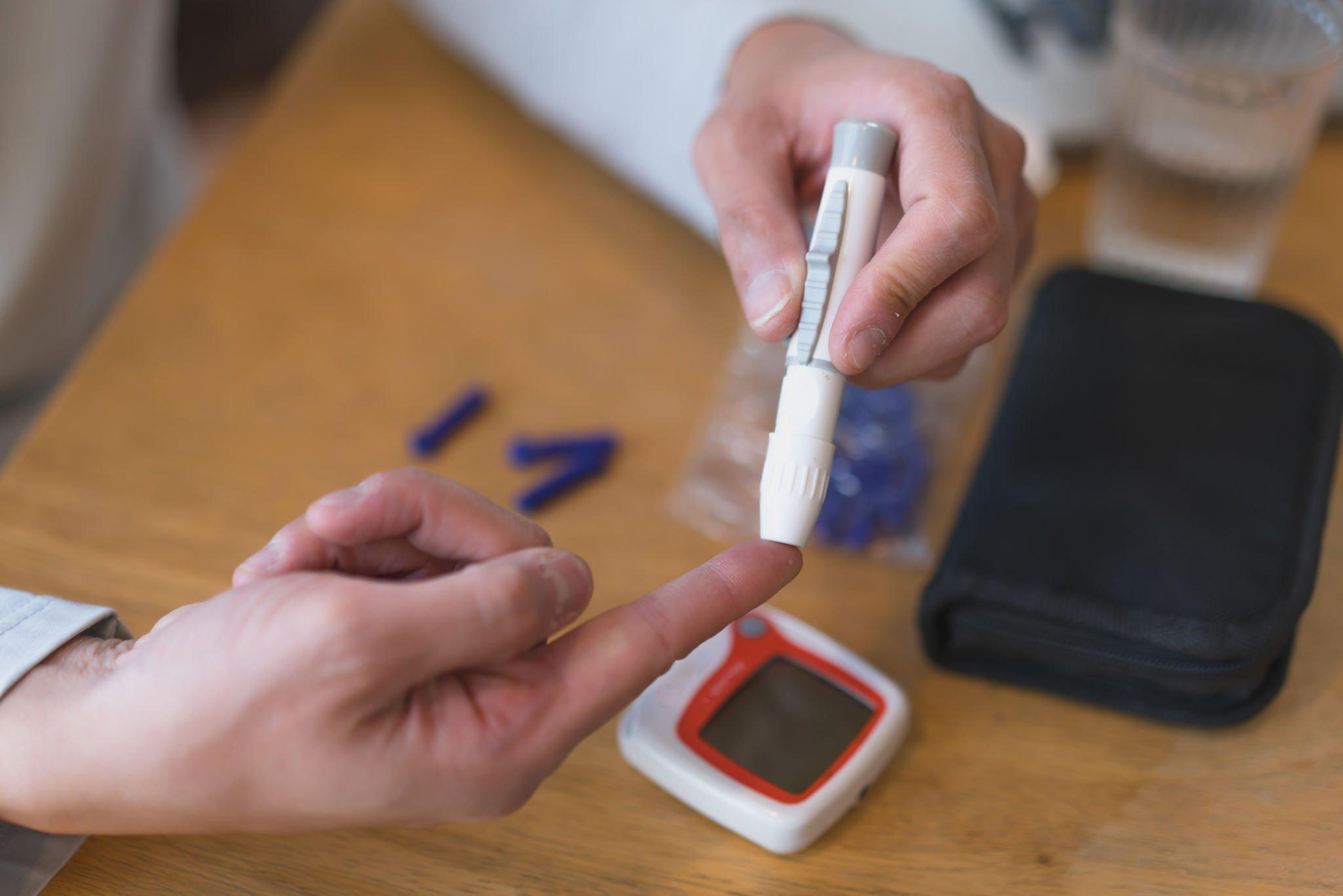 A person pricking their finger to perform a blood test, specifically a random blood sugar test, for the diabetes diagnosis by measuring blood sugar level.