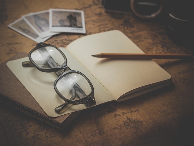 A notebook, pen, and glasses on a map representing travel writing.