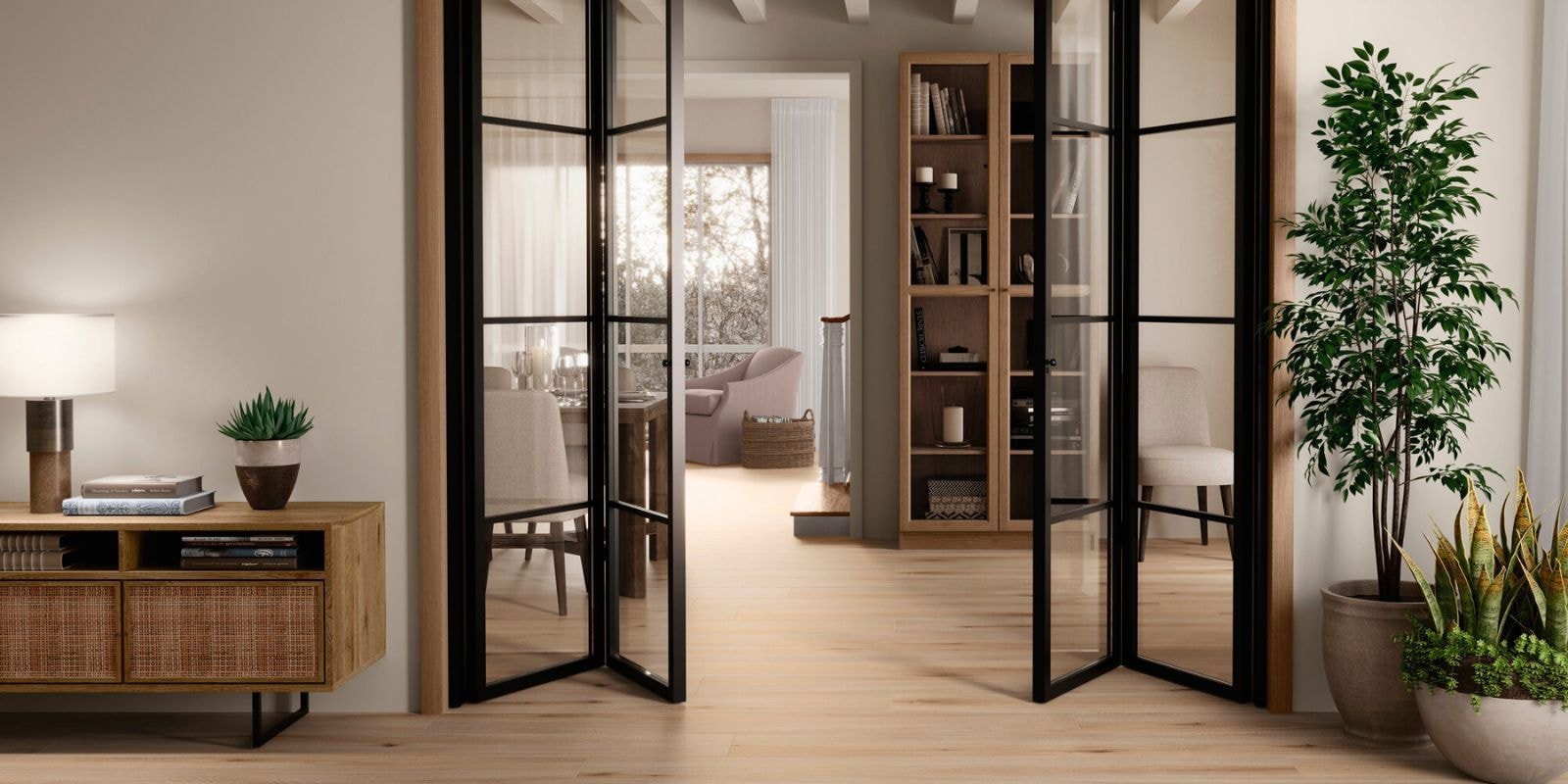 Bright and airy living space featuring light wood flooring, black-framed glass doors, indoor plants, and natural wood furniture with a cozy reading nook beyond.