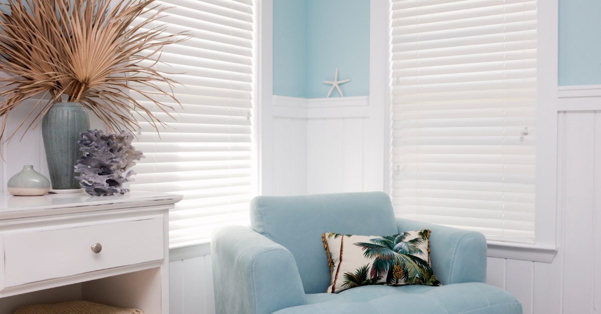 Bright coastal living room with soft blue walls, white trim, and a cozy chair accented by a tropical palm pillow — capturing the relaxed beach house vibe of Toms River NJ vacation rentals.