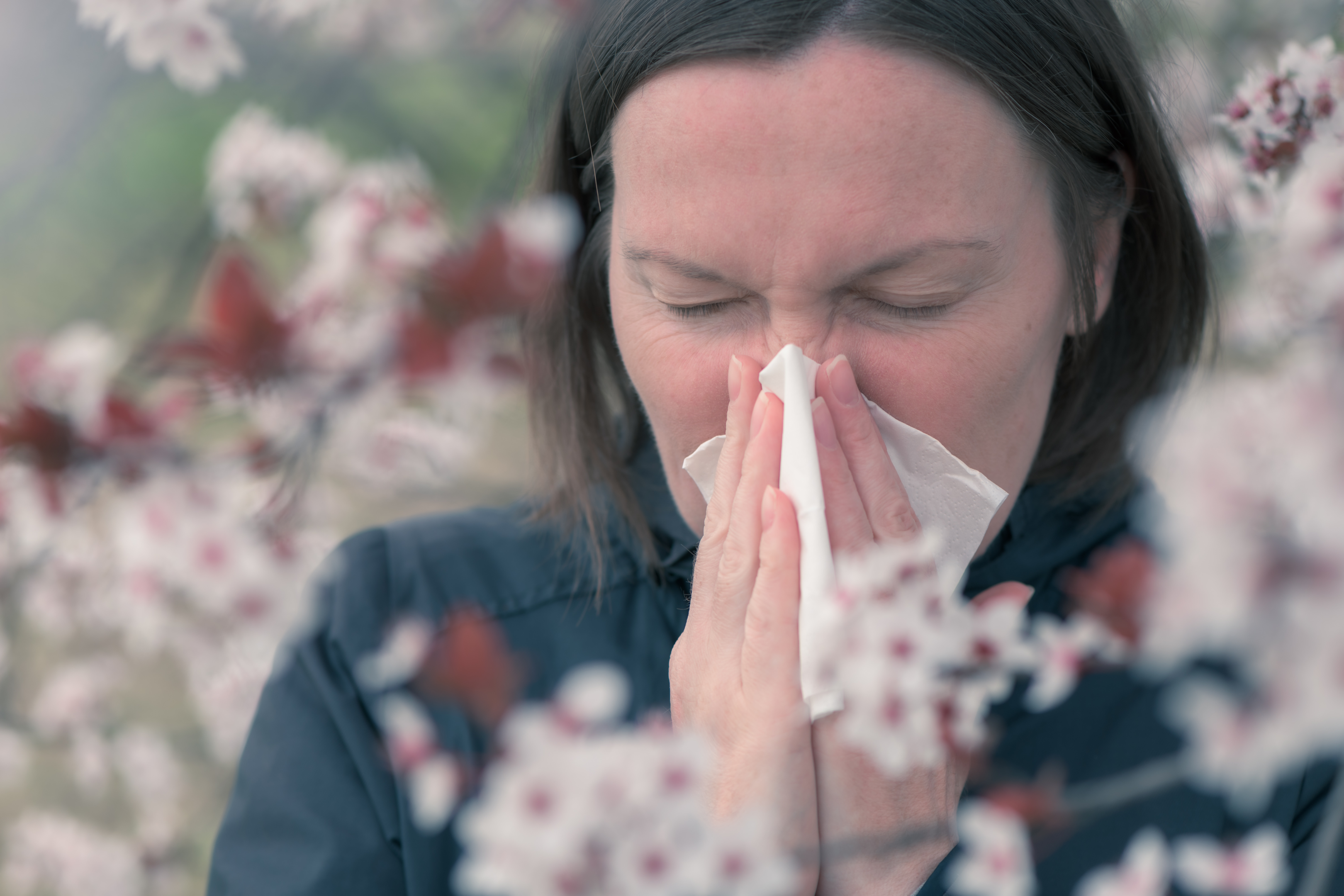 An image of a woman with seasonal allergies blowing her nose into a tissue. 