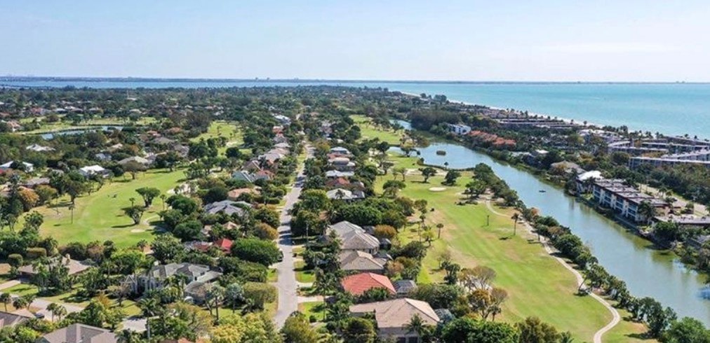 The image depicts tennis courts featuring a viewing deck and covered seating areas, set against the backdrop of the luxurious tropical island life on Sanibel Island. Surrounding the courts are beautifully landscaped grounds, adding to the serene atmosphere of this prime central Sanibel location.