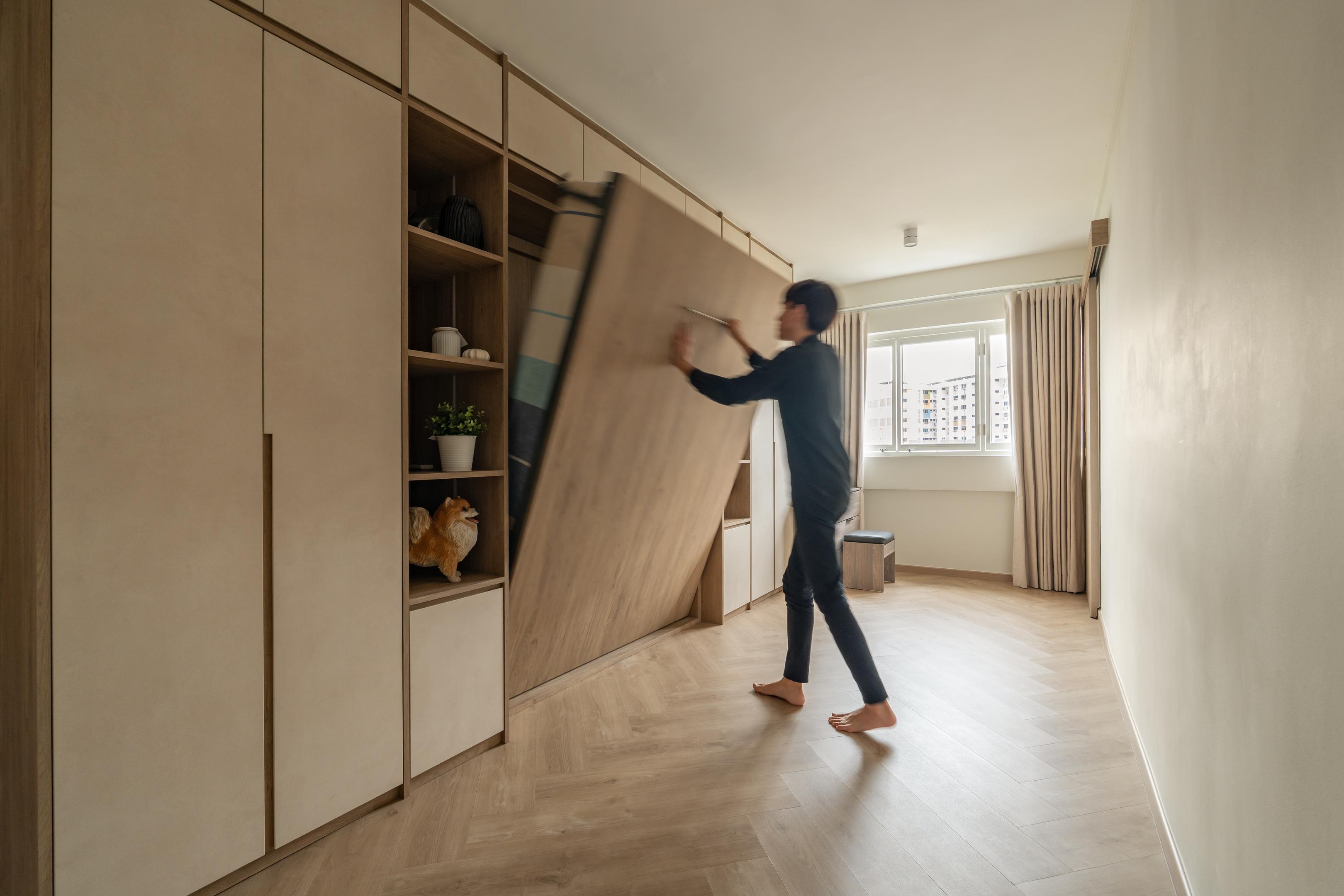 Modern Japandi interior featuring a built-in light wood wardrobe with a hidden bed being folded into the wall over herringbone flooring.