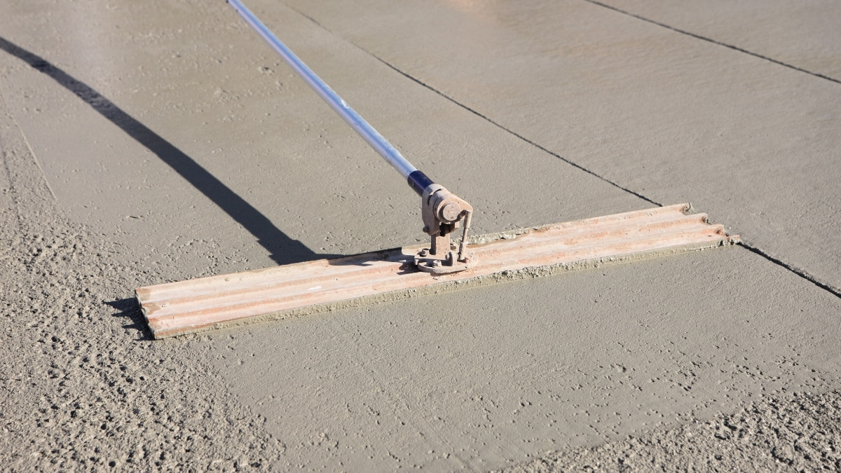 Worker transitioning from strike off bar to bull float on concrete surface