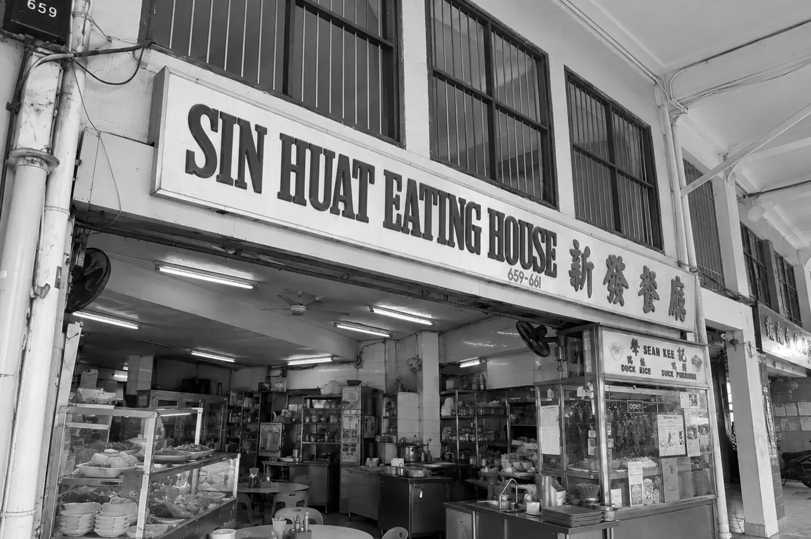 Front view of Sin Huat Eating House featuring its large traditional signboard, open-front dining space, food display counters, and simple interior seating.