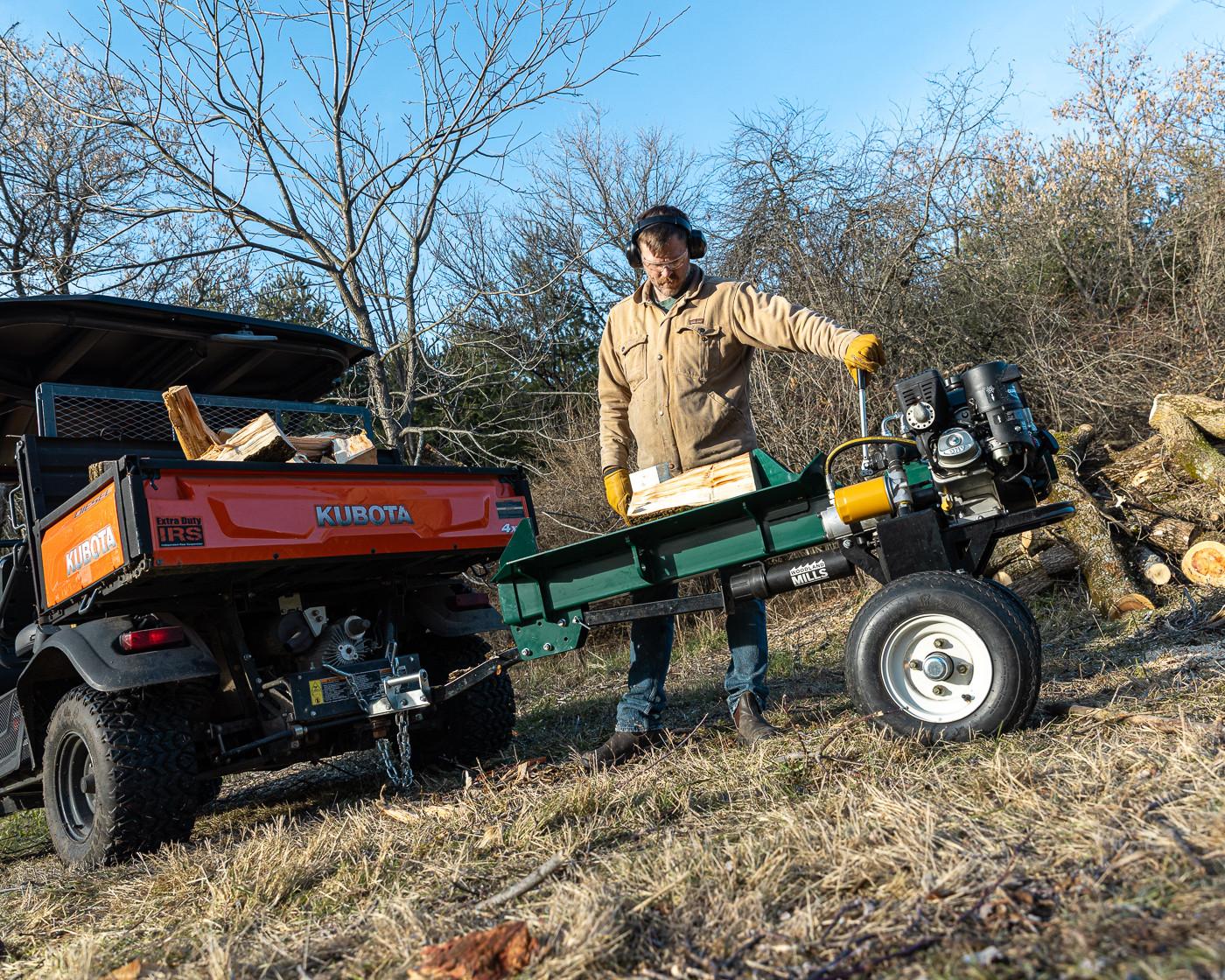 A man operating a Woodland Mills LS218 2-Way Log Splitter attached to a trailer filled with firewood.