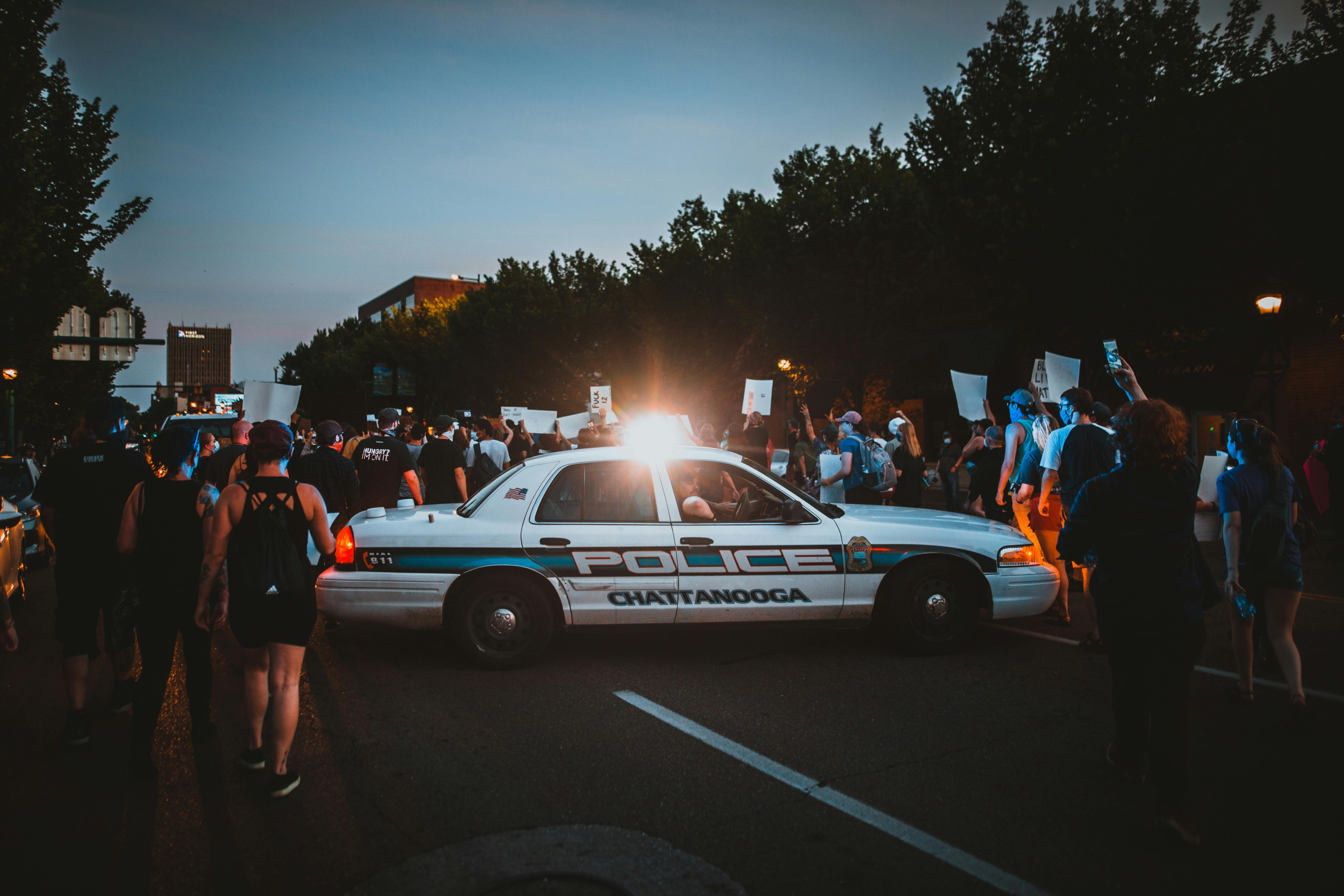 a crowd of people surround a police car during an outdoor demonstration