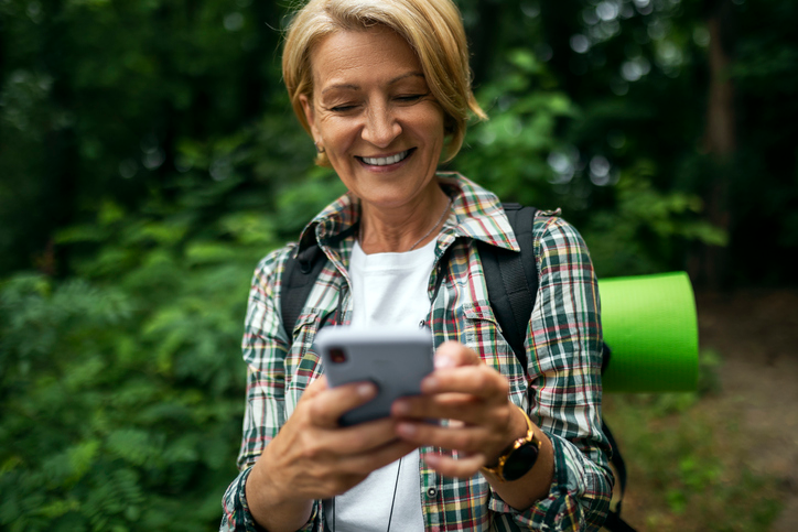 Woman in a plaid shirt carrying a backpack checking her text messages. 