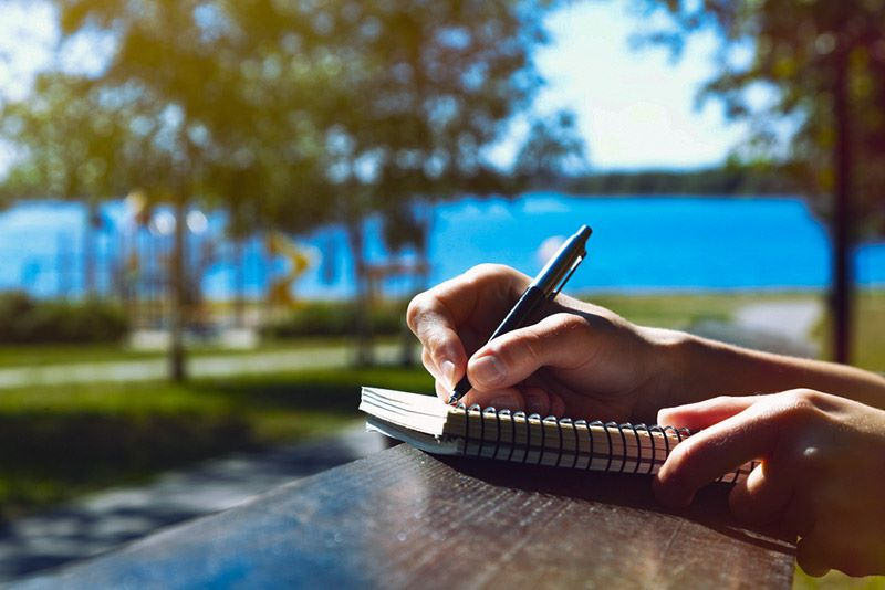 a person journalling on a wooden table, by a lake 
