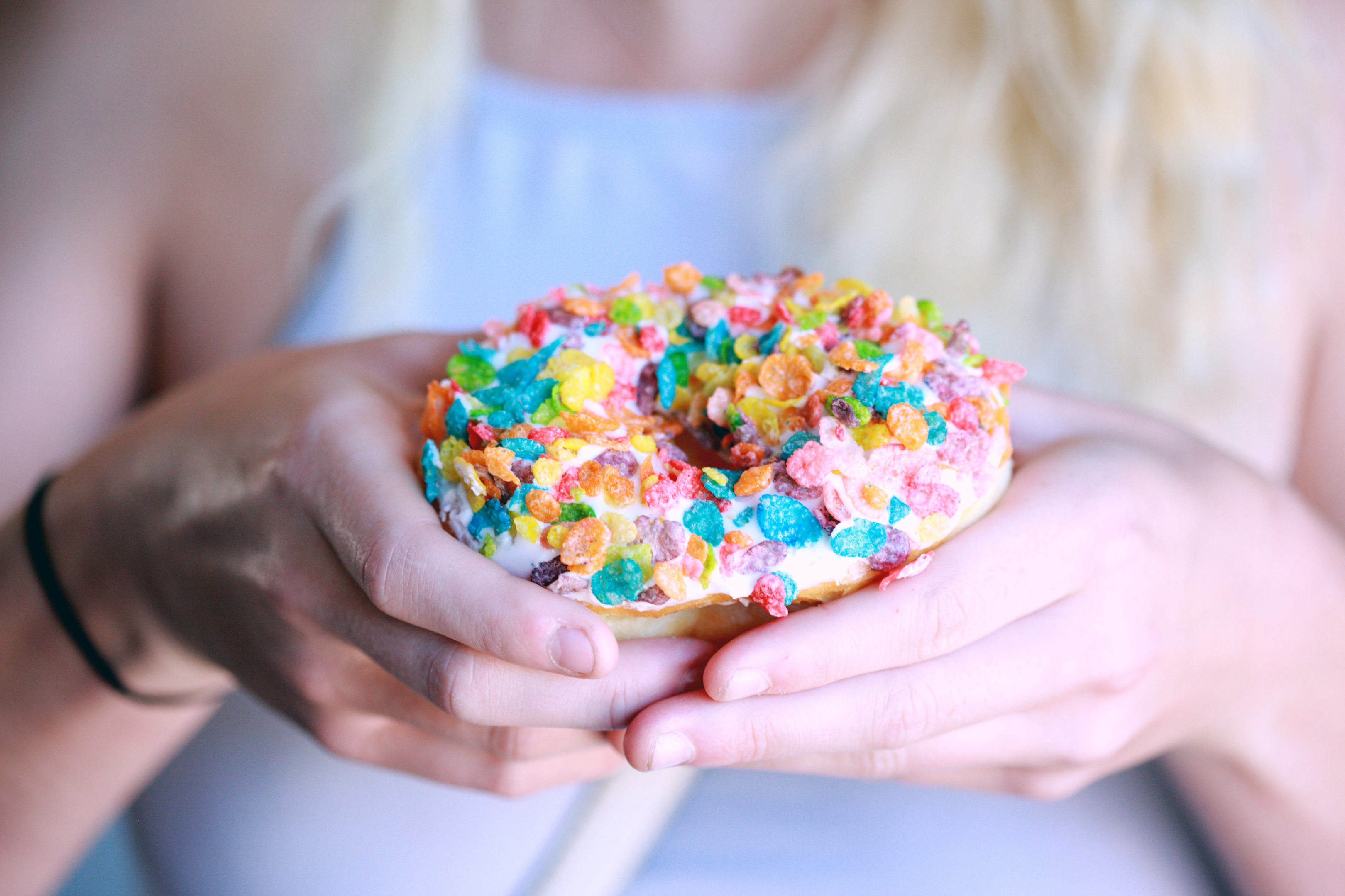 A picture of a woman's hand holding a doughtnut carefully with frosted colorful flakes. 
