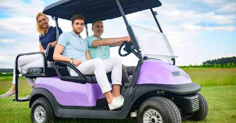 Two guys in front and one female in back in a purple golf cart in the country.