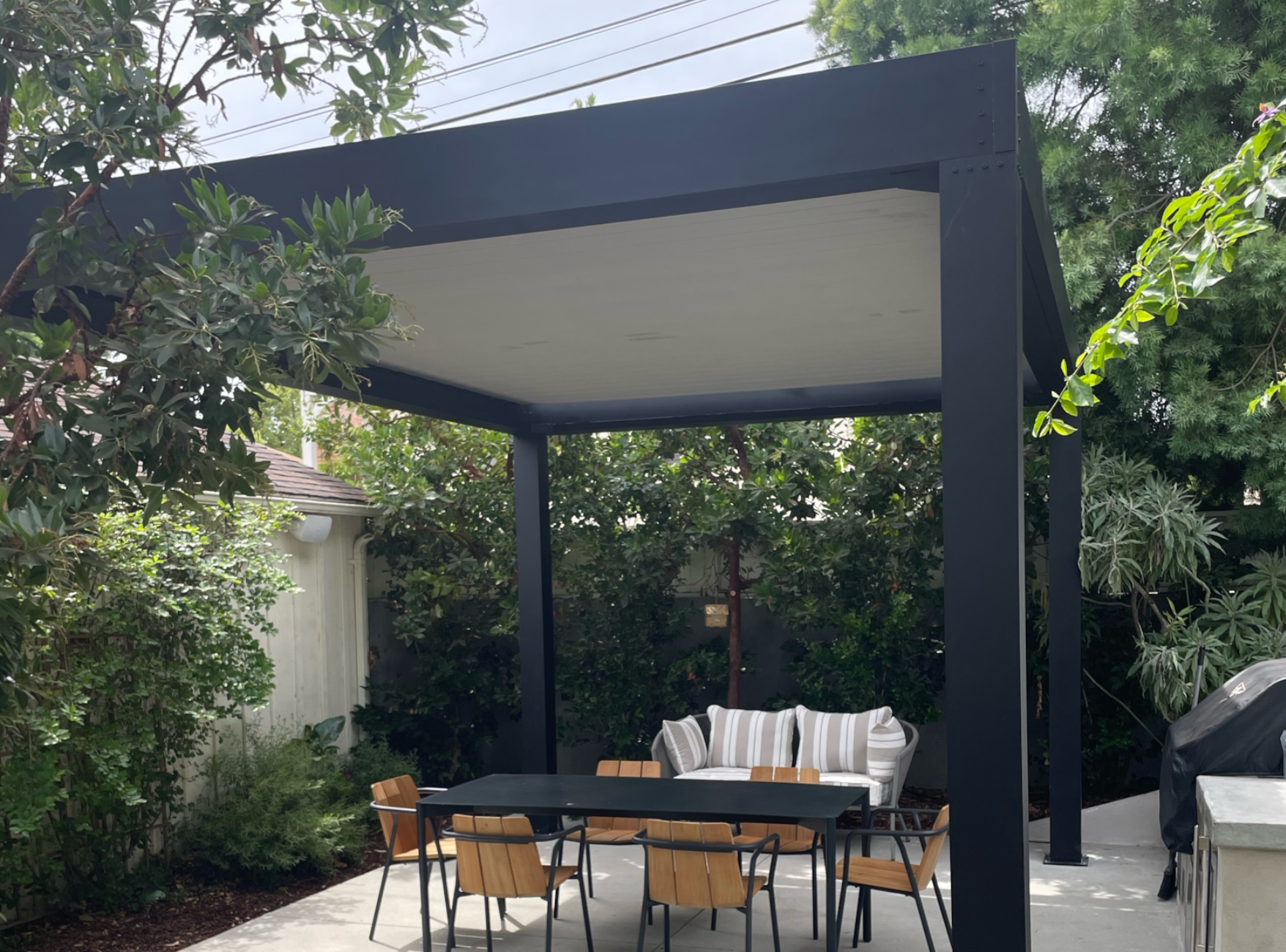 Freestanding black pergola with white louvers installed over a patio.