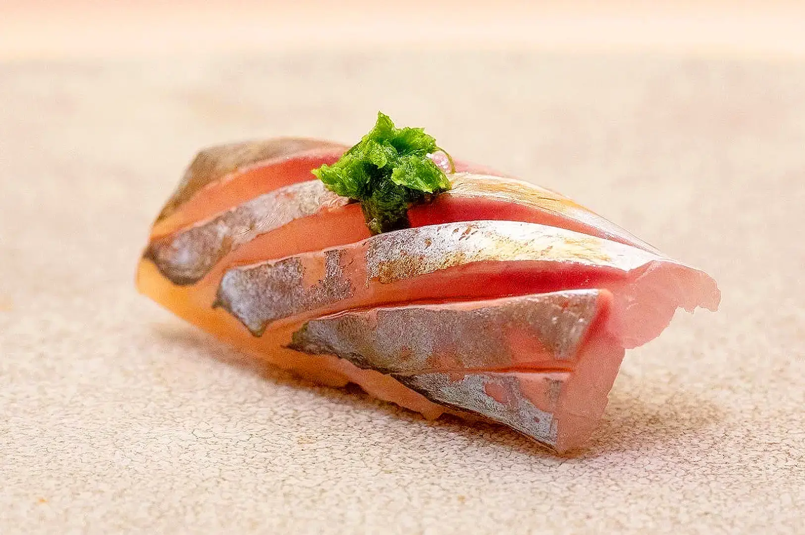 Fresh fish sushi nigiri with silver-skinned fish and shiso garnish at a premium omakase restaurant in Singapore