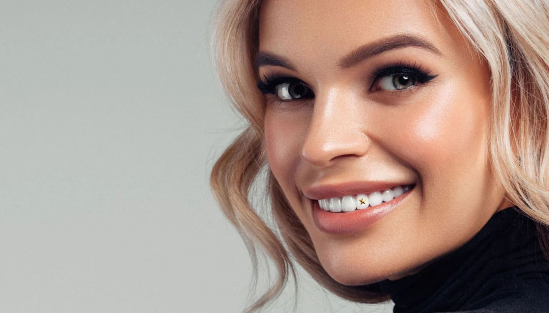 Tannsmykke: En liten detalj som gir stort smil 13 Kvinne med lyst hår smiler og viser tannpynt, en liten gullstjerne festet på tannen.