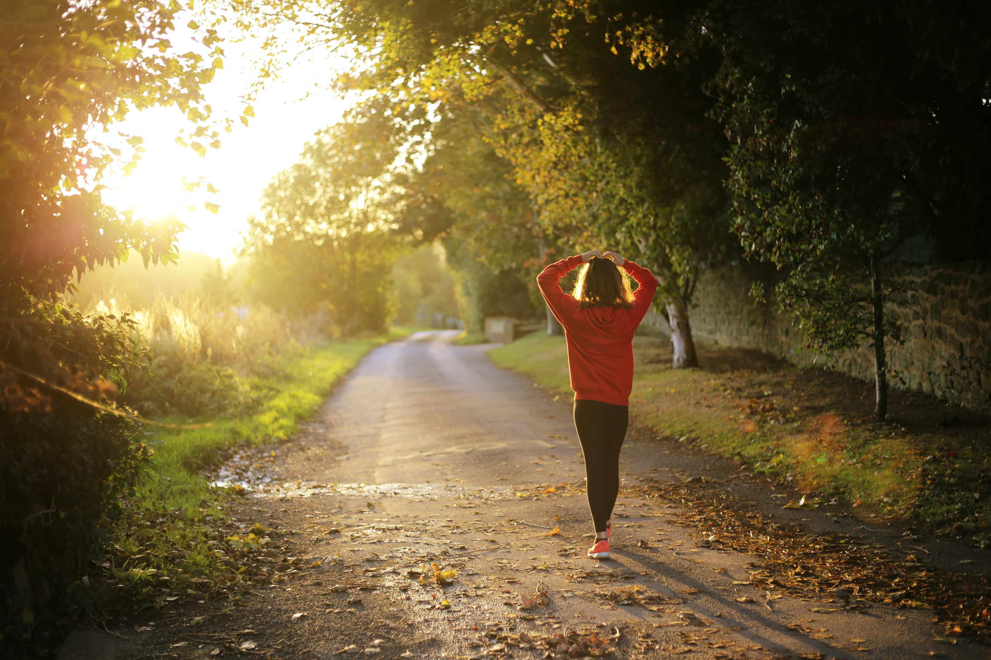 woman walking with her hands on her head in sunlight on a road in autumn