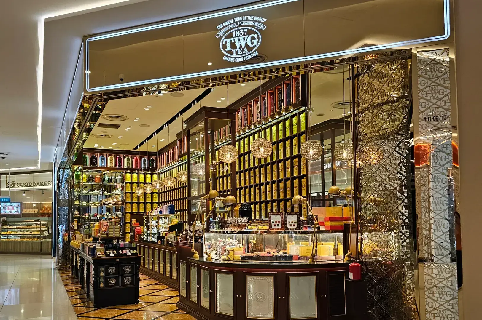 TWG Tea boutique with floor-to-ceiling tea tin displays, ornate columns, central counter, and luxury retail interior.