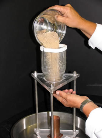 A cylindrical measure filled with fine aggregate sample and a funnel emptying out the sample