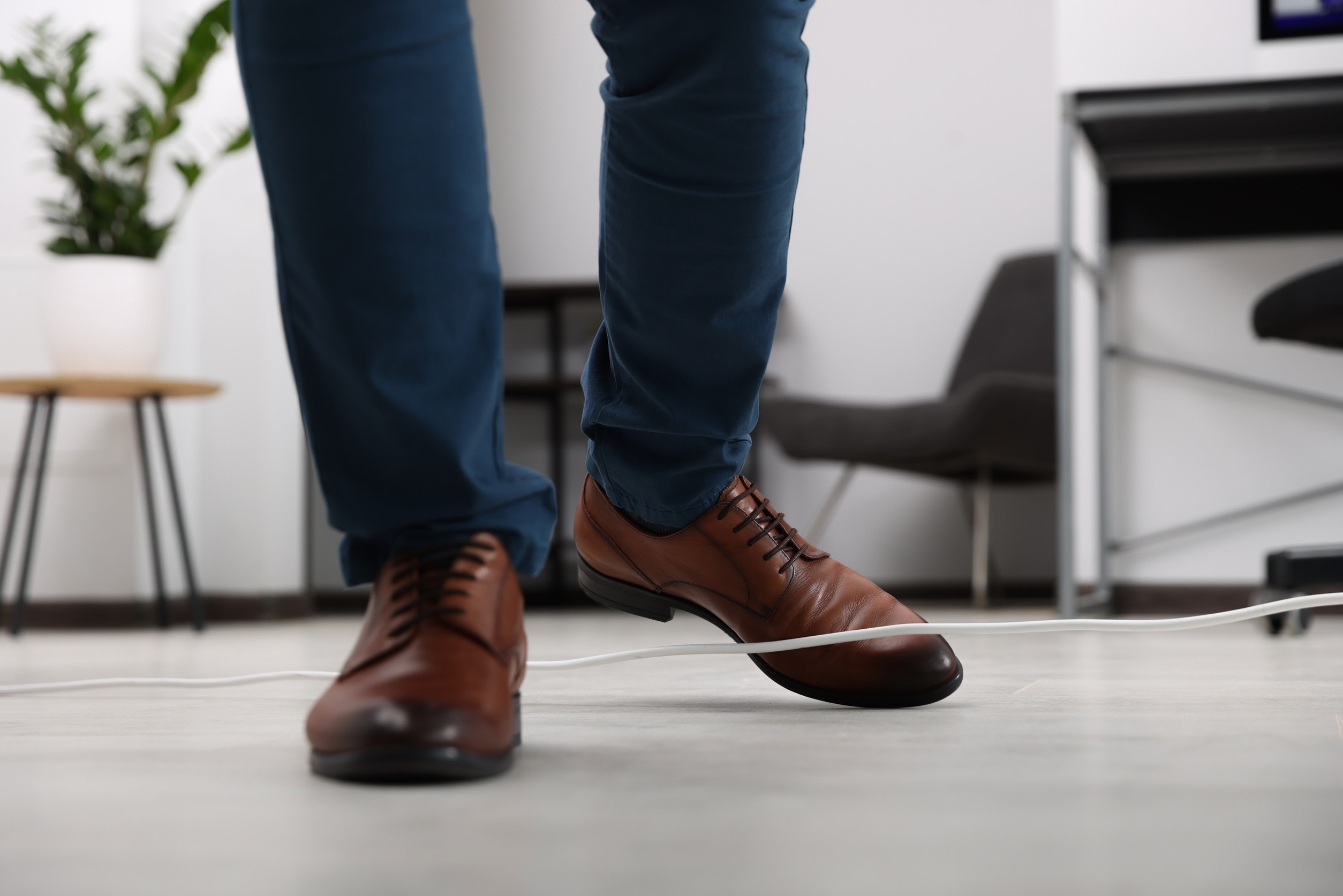 A man in brown shoes trips over a trailing wire in an office space