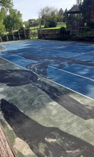 Worn-out tennis court with faded paint, visible cracks, indicating the need for resurfacing and repair.