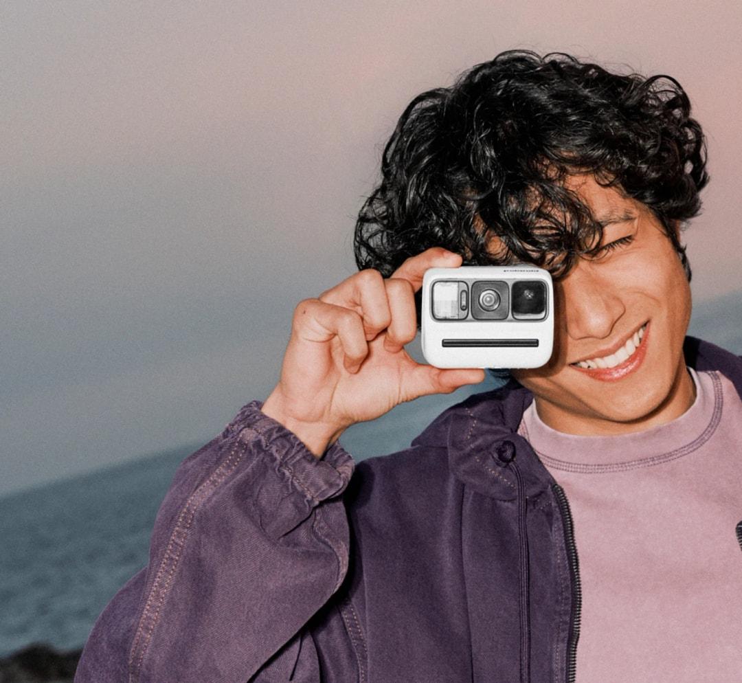 A lady holding the new Polaroid Go Generation 3 clipped to a backpack, next to compact travel gear, ready for spontaneous photography adventures.