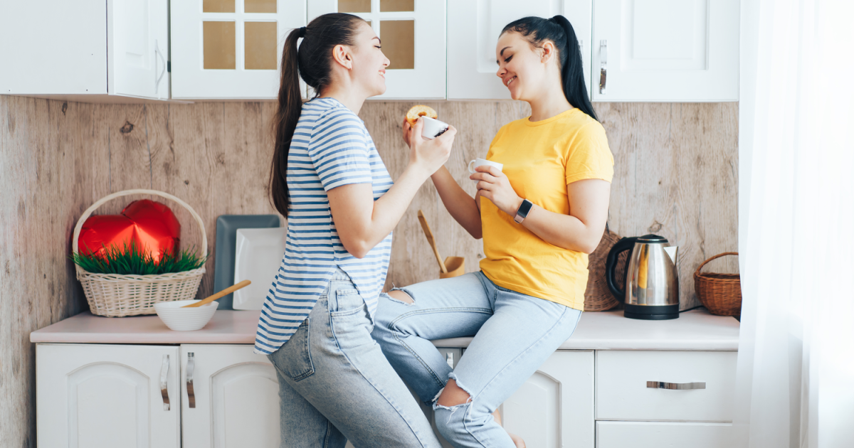 A content lesbian couple in New York City, enjoying quality time together while doing laundry, having experienced the benefits of sex and schema therapy at GayCouplesTherapy.com, resulting in a more fulfilling and satisfying sex life, strengthening their emotional bond in everyday activities.